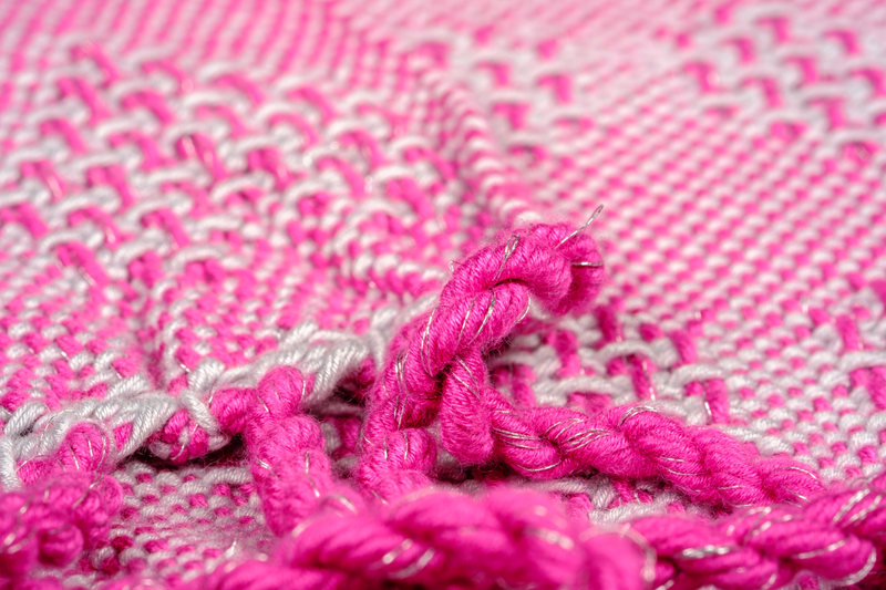 Close-up of the fringes of a handwoven shawl in bamboo pink and a silver sewing thread