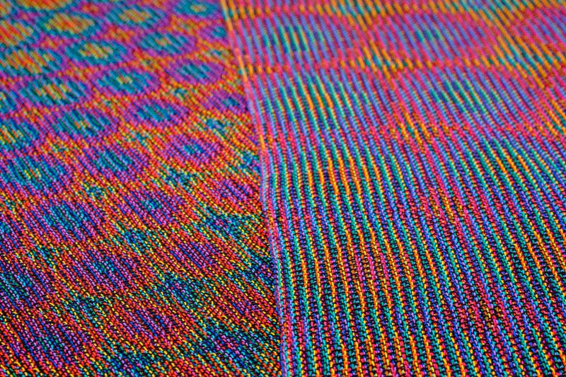 Another close-up of two shawls in echo weave techniques using rainbow colors folded onto one another