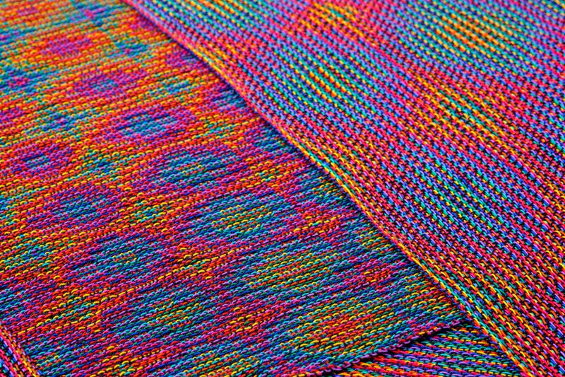 Close-up of two shawls in echo weave techniques using rainbow colors folded onto one another