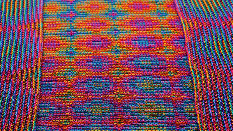 Close-up of two shawls in echo weave techniques using rainbow colors at a low angle