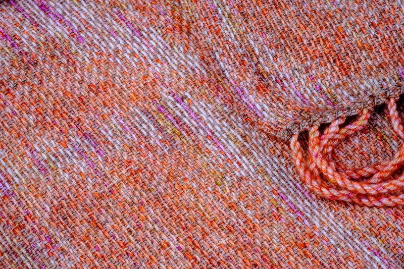 Close-up of the fringes on a handwoven shawl in reddish orange